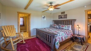 A bedroom with a wooden bed, a rocking chair, a ceiling fan, and a rug.