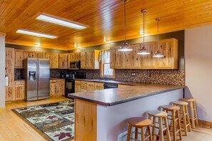 A modern kitchen with wooden cabinets, a stainless steel refrigerator, and a central island with bar stools.