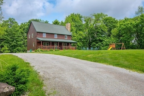 A two-story log cabin with a porch, surrounded by a grassy yard and trees. - Dragonfly Lodge | Hocking Hills, 5BR, Hot Tub (Logan)