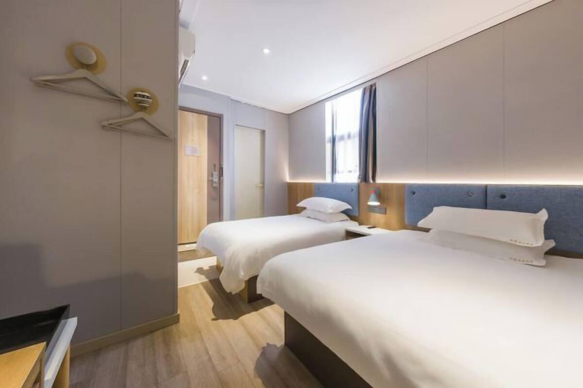 A hotel room with two beds, a wardrobe, a mirror, and a window.