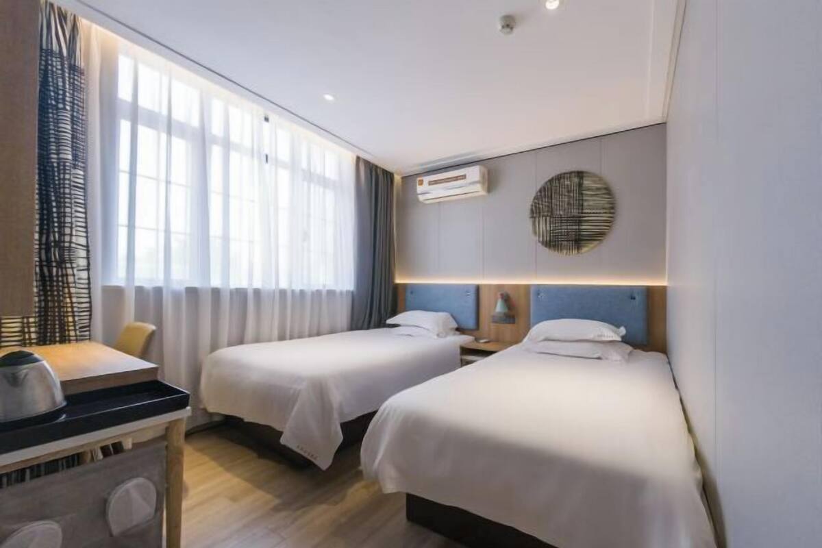 A hotel room with two beds, a desk, a chair, and a window with curtains.