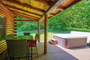 A covered outdoor deck with a hot tub, wooden chairs, and a table.
