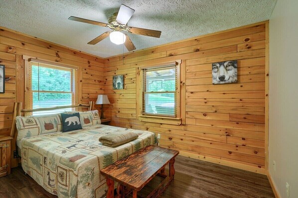 Ein gemütliches Schlafzimmer im Chalet-Stil mit Bett, einer Bank, zwei Fenstern, einem Deckenventilator und Holzwänden.
