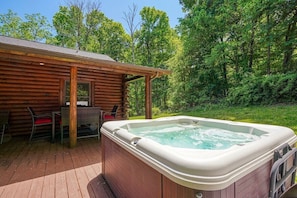 Eine Holzhütte mit Whirlpool auf einer Terrasse, umgeben von Bäumen.