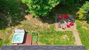 An aerial view of a backyard with a hot tub, outdoor seating area with red chairs, and a fire pit.