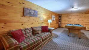 Una habitación acogedora con un sofá de cuadros, una mesa de billar, paredes de madera y una lámpara en el techo.