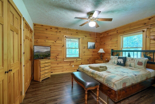 A wooden cabin bedroom with a bed, bench, ceiling fan, and two windows. - Amazing Starr Cabin | Hocking Hills, Hot Tub, 3BR (Rockbridge)