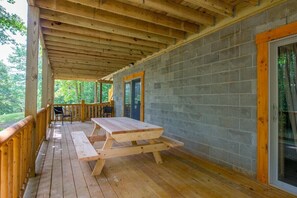Um deck de madeira coberto com uma mesa de piquenique e cadeiras, uma parede de tijolos e uma porta de vidro.