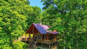 A cabin with a wooden exterior, a red roof, and a deck with stairs leading to the entrance.