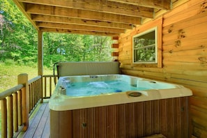 Une cabane en bois dotée d’un jacuzzi sur une terrasse, entourée d’arbres.