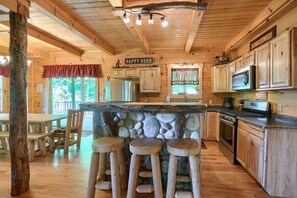 Een rustiek houten cabin interieur met een stenen bar, houten krukken, een keuken met houten kasten en een eethoek met een rood gordijn.