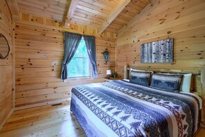 A wooden cabin bedroom with a bed, curtains, a wall-mounted plant, and a bedspread.