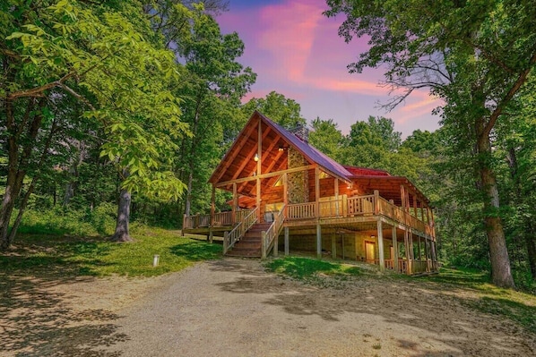 Une cabane en bois dotée d’une véranda et d’un escalier, entourée d’arbres.