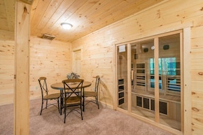 A wooden cabin interior with a dining table and chairs, a carpeted floor, and a sliding glass door leading outside.