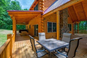Eine Holzhütte mit überdachter Terrasse, Sitzgelegenheiten im Freien und einer Steinmauer.