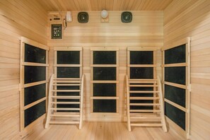 Uma sala de sauna com paredes e bancos de madeira, um painel de controle e três alto-falantes.