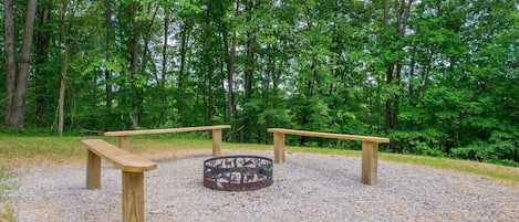A circular fire pit surrounded by wooden benches in a forested area.