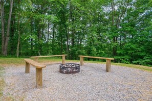 A circular fire pit surrounded by wooden benches in a forested area.