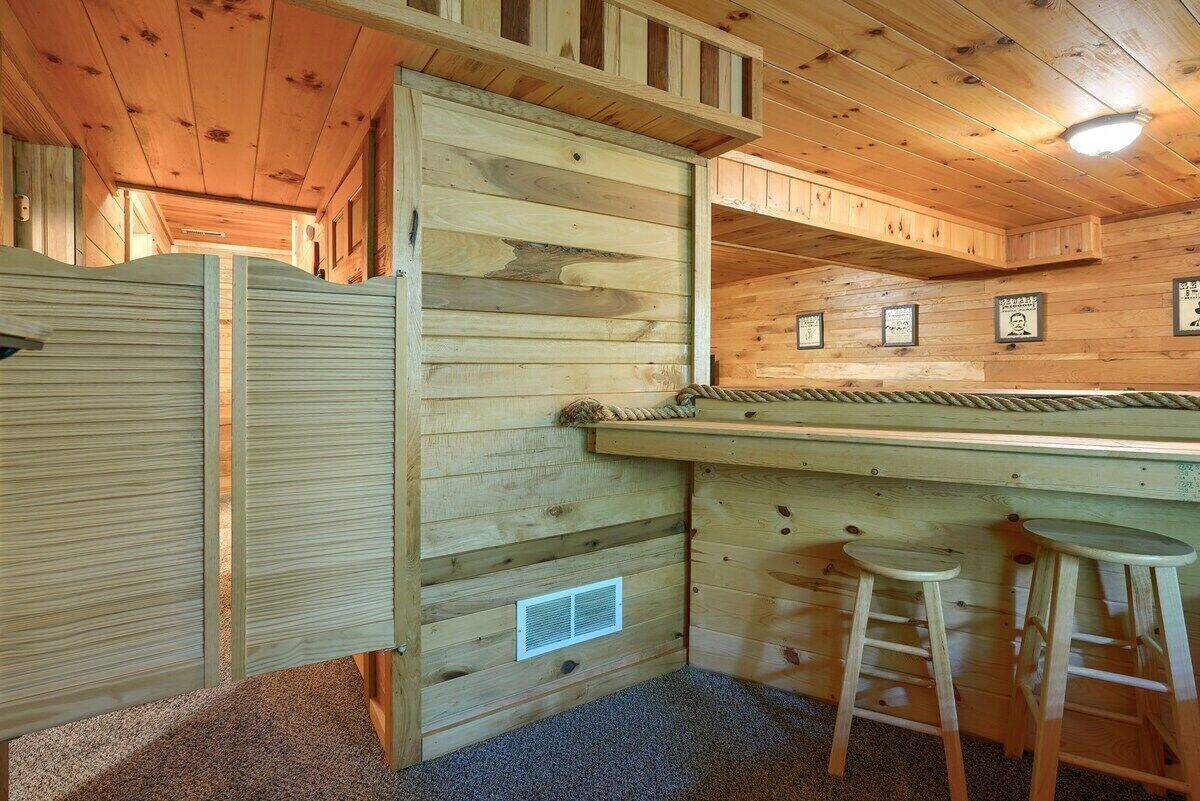 A wooden cabin interior with a bar area, stools, and a door.