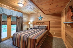 Un dormitorio de cabaña de madera con una cama, cortinas, un adorno de estrella y una mesita de noche con una lámpara.