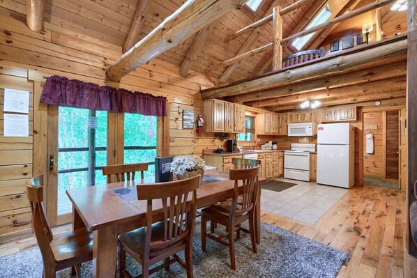 Una cabaña de madera con comedor, cocina y habitación en un altillo.