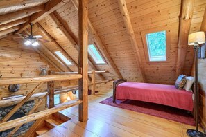 A cozy attic bedroom with a wooden ceiling, a bed with a red bedspread, and a skylight.