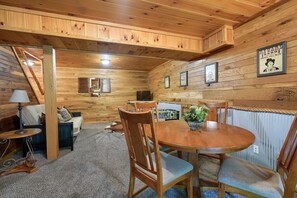 A cozy wooden cabin interior with a dining area, a sofa, and a lamp. - Hickory House | Hocking Hills, 30 Acres, Pets (Logan)