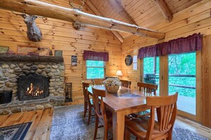 A wooden cabin interior with a stone fireplace, a dining table, and chairs.