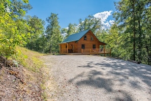 A wooden cabin with a gravel driveway, surrounded by trees.