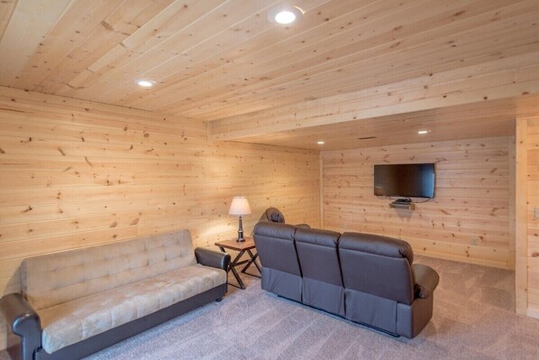 A cozy room with a sofa, a chair, a small table with a lamp, and a TV mounted on the wall.