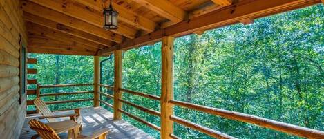 A wooden deck with a railing, wooden chairs, and a hanging lantern.