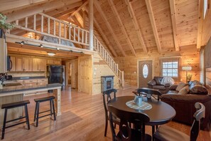 A spacious cabin interior with a dining area, kitchen, and a loft bedroom. - Buck Ridge Cabin | Hocking Hills, 12 Acres, Pets (Rockbridge)