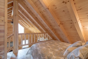 A wooden attic bedroom with a bed, a wooden staircase, and a sloped ceiling.