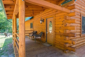 Eine Blockhütte mit Veranda, einer Tür mit Fensterglas und zwei Korbstühlen.