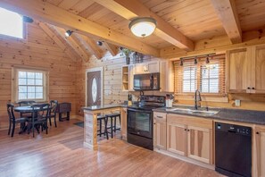 A log cabin with a kitchen featuring wooden cabinets, a stove, and a dishwasher.