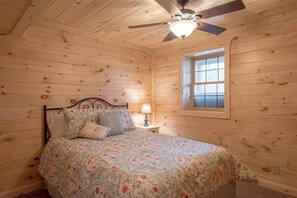 A wooden-paneled bedroom with a bed, a nightstand, a ceiling fan, and a window. - Buck Ridge Cabin | Hocking Hills, 12 Acres, Pets (Rockbridge)