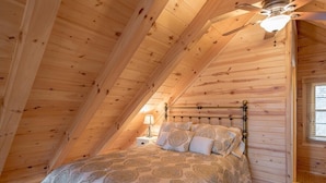 Une chambre avec un plafond en pente, un lit avec une literie à motifs, une table de chevet et un ventilateur de plafond.