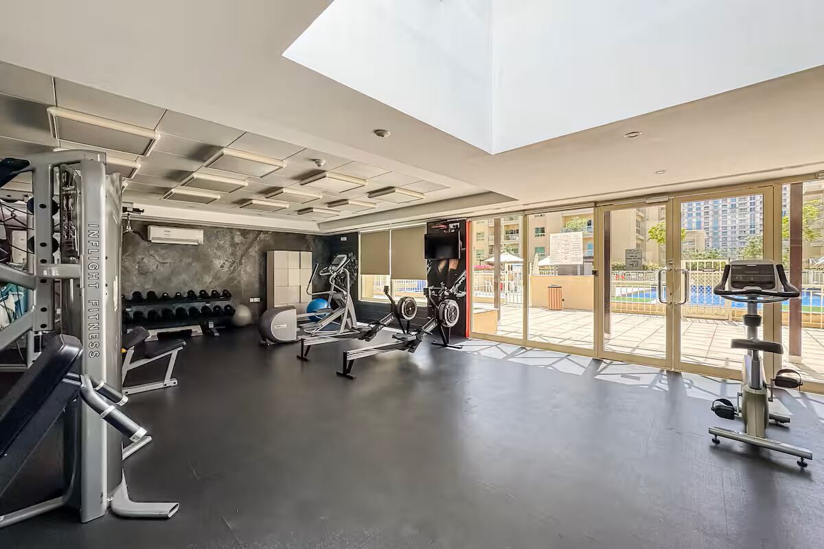A gym with various exercise equipment, large windows, and a view of buildings outside.