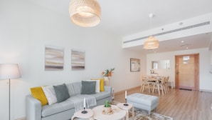 Una sala de estar moderna con un sofá gris, una zona de comedor con una mesa y sillas de madera, y una cocina visible al fondo.