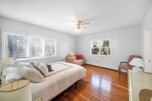 A bedroom with a bed, bedside lamps, a ceiling fan, and two windows with blinds. - Classic Cape Escape in Charming Cotuit (Contuit)
