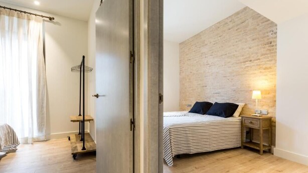Una camera da letto con un letto, un comodino, una lampada, un pavimento in legno, una parete in mattoni e una porta.