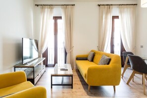 Een woonkamer met een gele bank, een salontafel, een tv op een dressoir en een stoel.