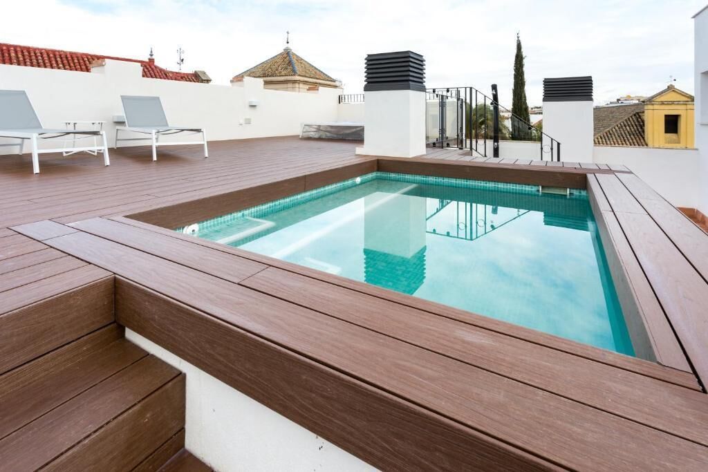 Swimmingpool på taget med træterrasse og hvide liggestole.