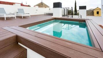 Une piscine sur le toit, dotée d’une terrasse en bois et de chaises longues blanches.