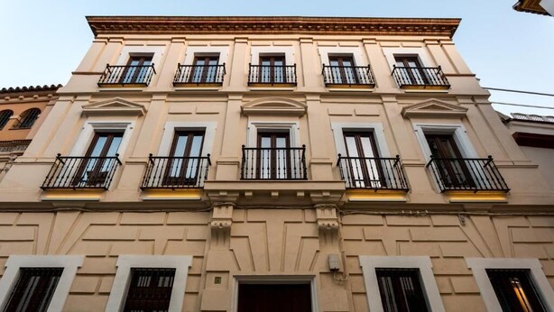 Un edificio de varios pisos con fachada simétrica, ventanas regularmente distribuidas y balcones con barandillas negras.