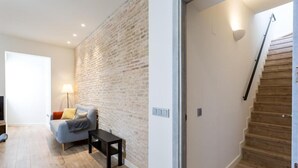 A modern living room with a brick wall, a sofa, a small table, and a staircase with wooden steps.
