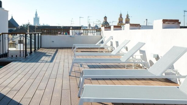 A rooftop terrace with wooden flooring and white sun loungers.