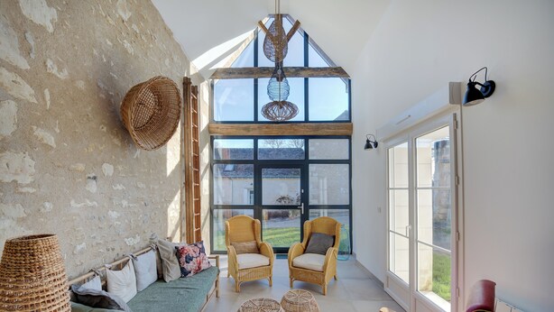 A cozy room with a high ceiling, wicker furniture, and a large window offering a view of the outdoors. - Domaine des Cyclamens (Verneuil-sur-Indre)