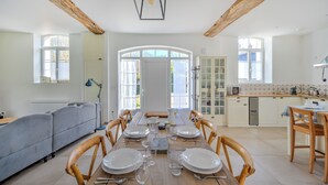 A dining area with a wooden table set for six, surrounded by wooden chairs. There is a kitchen area with white cabinets and a countertop visible in the background. - Domaine des Cyclamens (Verneuil-sur-Indre)