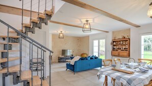 A spacious living area with a modern staircase, a blue sofa, and a dining table set for four. - Domaine des Cyclamens (Verneuil-sur-Indre)